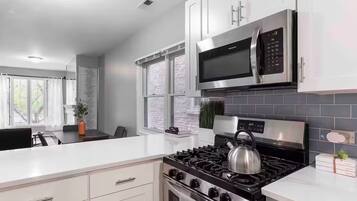 A modern kitchen with white cabinetry, a stainless steel stove, a microwave, and a gas range.