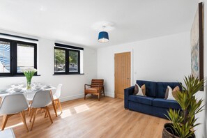 Ein modernes Wohnzimmer mit Essbereich, einem blauen Sofa und einer Holztür.