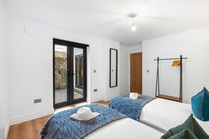 Une chambre d’hôtel dotée d’une grande porte-fenêtre coulissante donnant sur un espace extérieur, d’un lit recouvert d’une couette blanche et d’une couvre-lit à motifs bleus, d’un plancher en bois et d’un ventilateur de plafond.