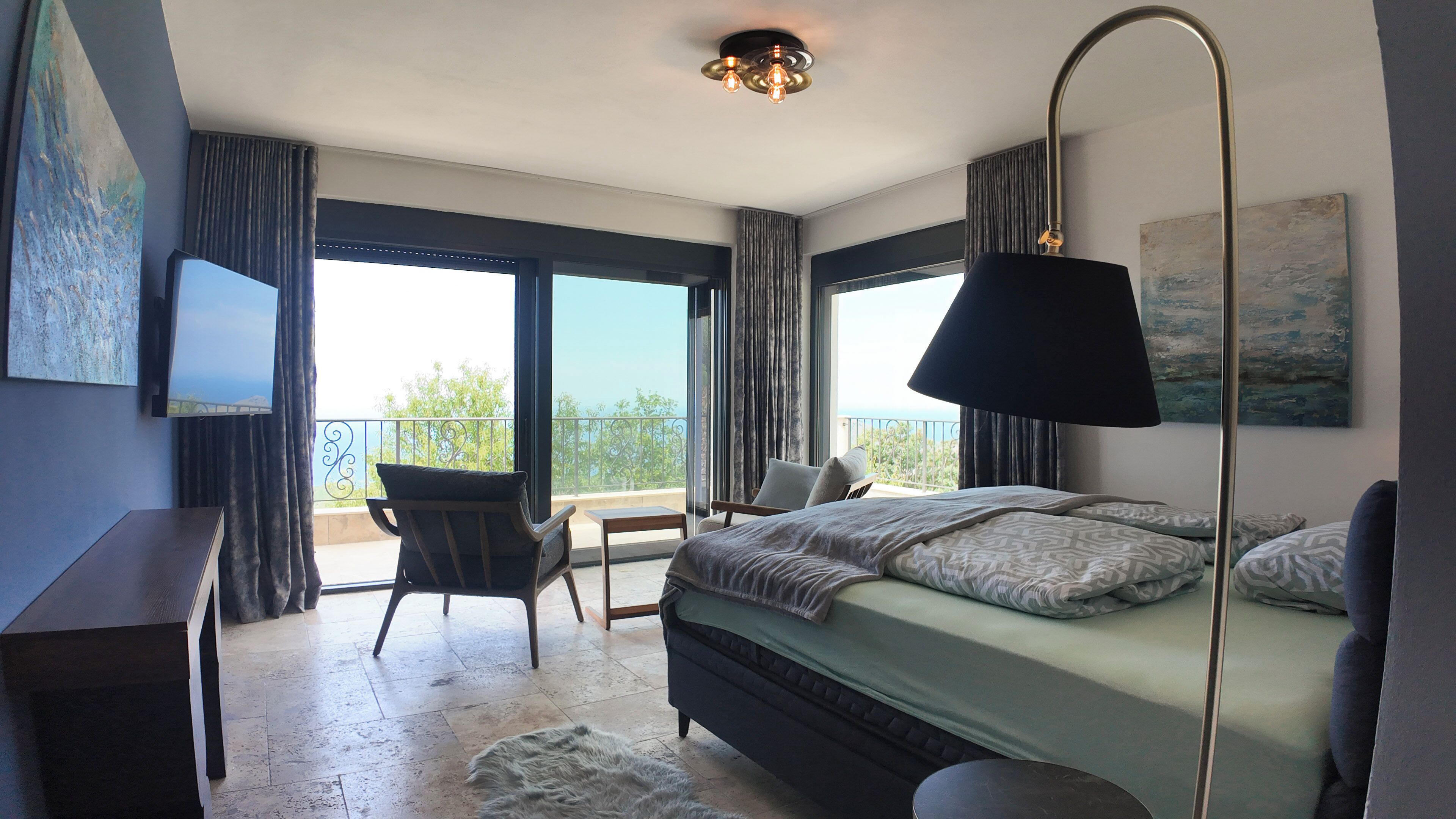 A bedroom with a bed, a chair, a desk, a lamp, and a balcony with a view.
