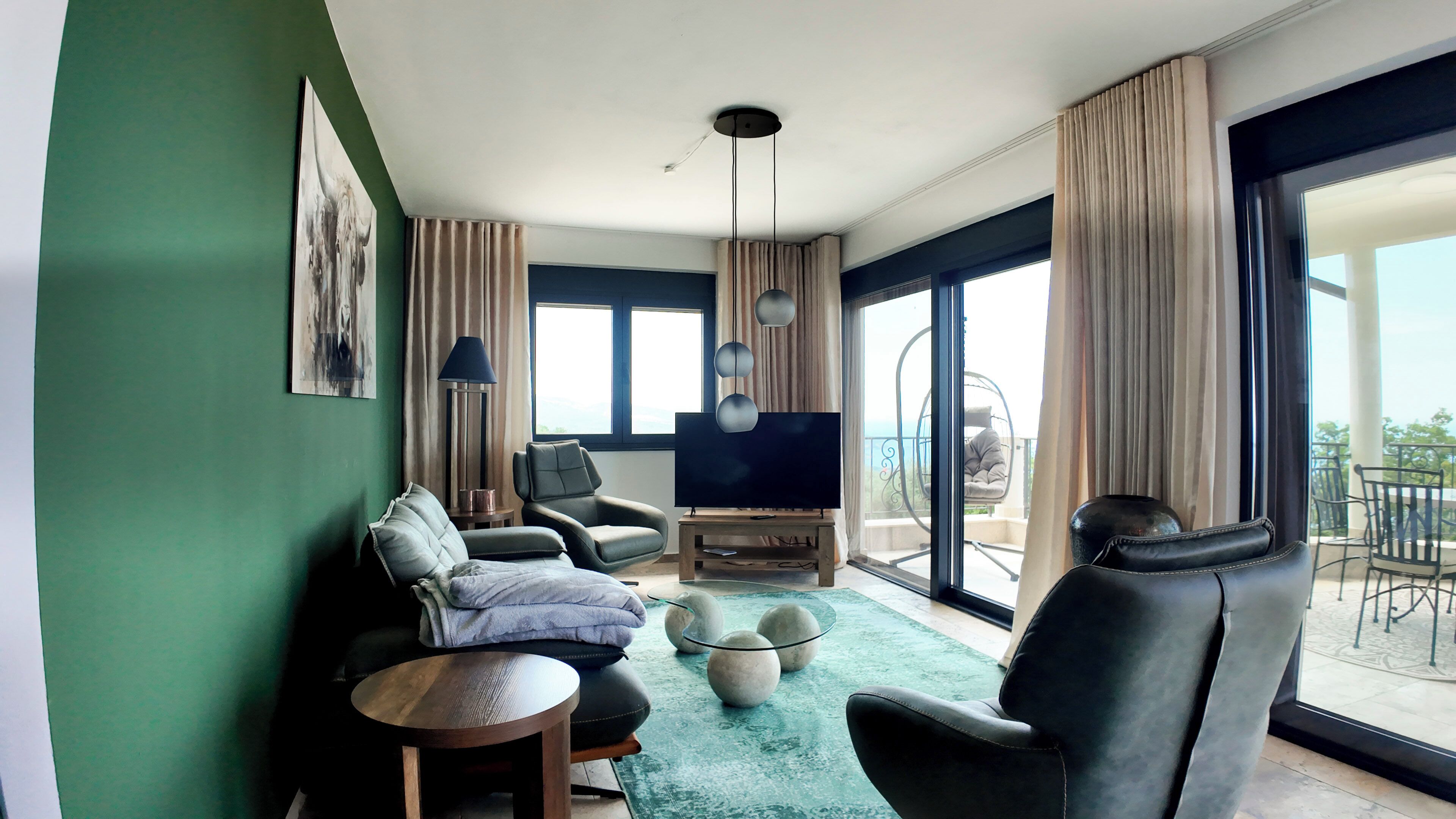 A modern living room with a sofa, chairs, a TV, and a balcony with outdoor seating.