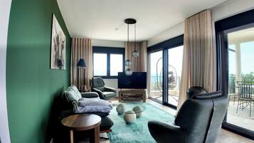 A modern living room with a sofa, chairs, a TV, and a balcony with outdoor seating.