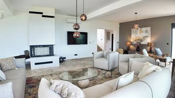 A modern living room with a glass coffee table, white sofas, and a flat-screen TV.