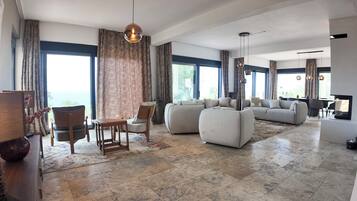 A spacious living room with a large sofa set, a dining area with a table and chairs, and a television.