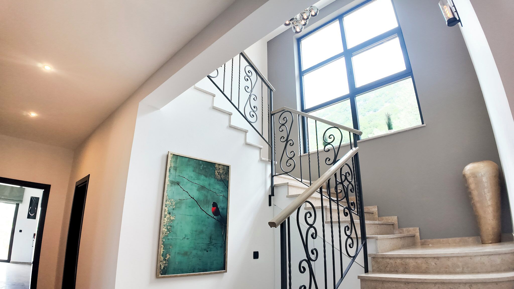 A staircase with a wrought iron railing, a large window, and a painting on the wall.