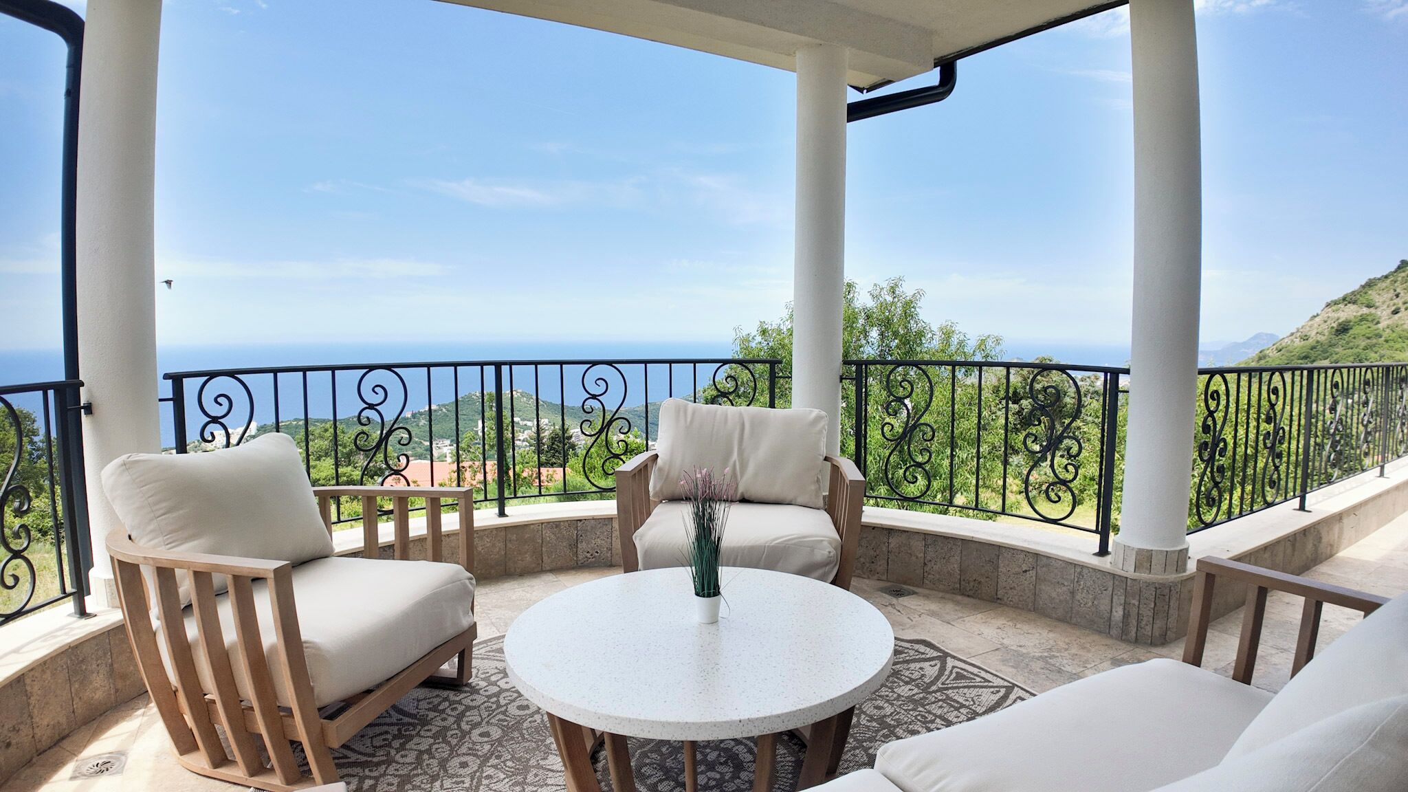 A covered outdoor seating area with a view of the sea and hills.