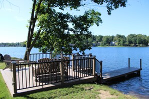 Ein Seeufer mit einer Holzterrasse, Adirondack-Stühlen und einem Steg, der ins Wasser führt.