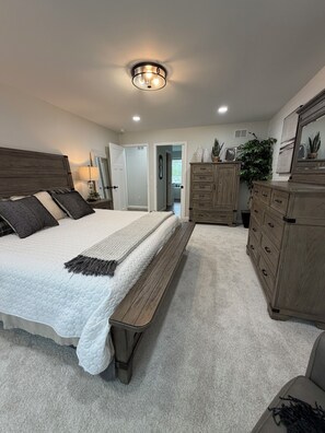 Ein Schlafzimmer mit einem großen Bett, einem Holzkopfstück, einer Bank, einem Schminktisch und einem Spiegel.