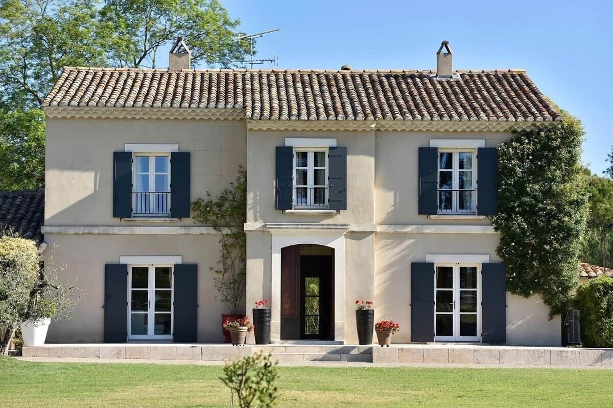 Una casa de dos pisos con techo de tejas, una entrada central y un pequeño porche con plantas en macetas.