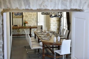 A dining area with a long wooden table set for six, surrounded by white chairs. - Mas Saint Jean - Domaine de Malaga - New Property (Maussane-les-Alpilles)