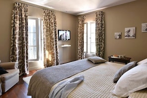 A bedroom with a bed, curtains, a television, a small table with a tray, and artwork on the wall. - Mas Saint Jean - Domaine de Malaga - New Porperty (Maussane-les-Alpilles)