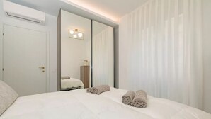 Une chambre d’hôtel avec un grand lit, un miroir, un climatiseur fixé au mur et une fenêtre avec des rideaux légers.