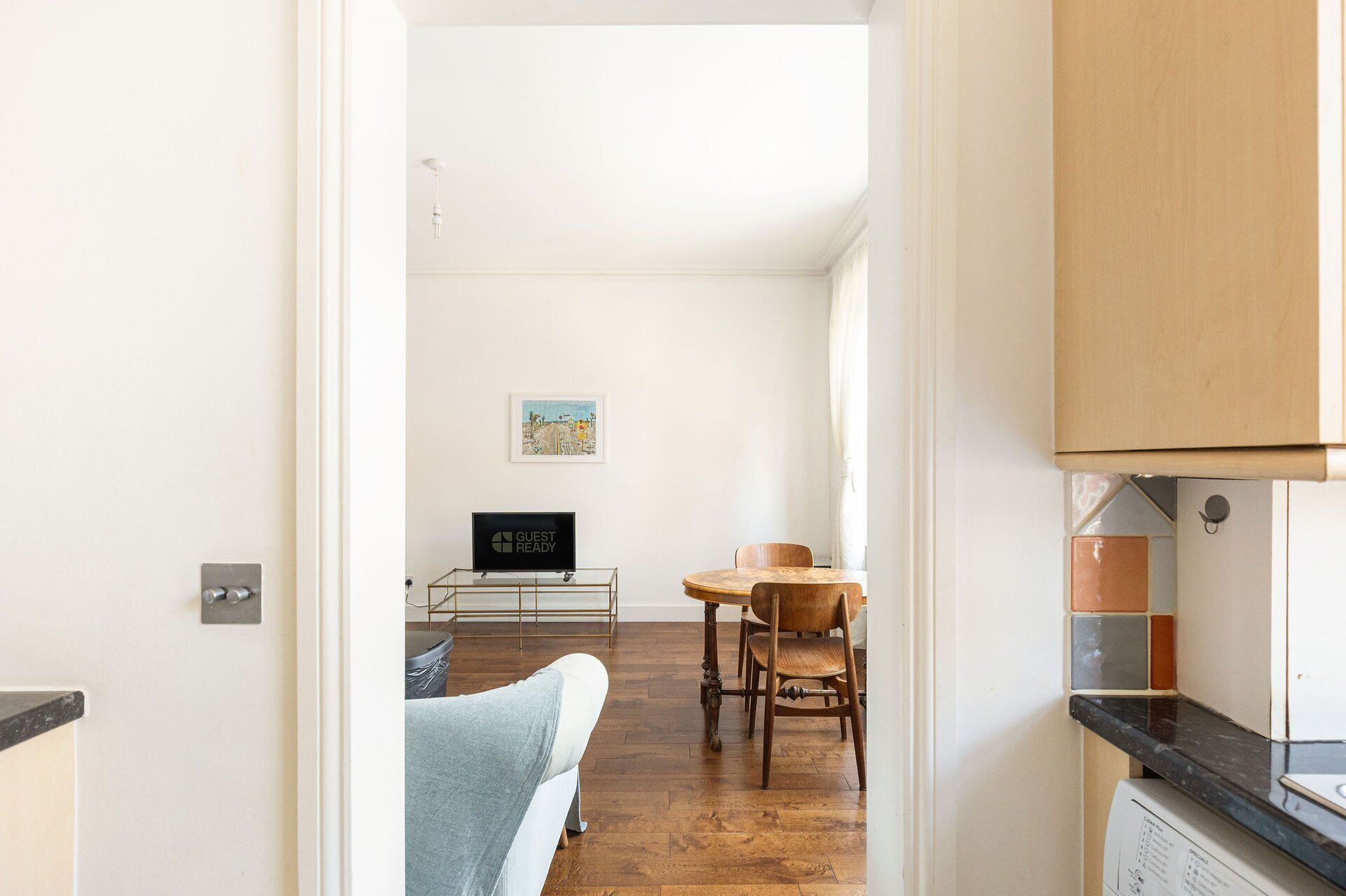 Une cuisine moderne avec une table et des chaises en bois, un panneau indiquant « PRÊT POUR LES INVITÉS » et une vue sur un coin repas doté d’un plancher en bois.