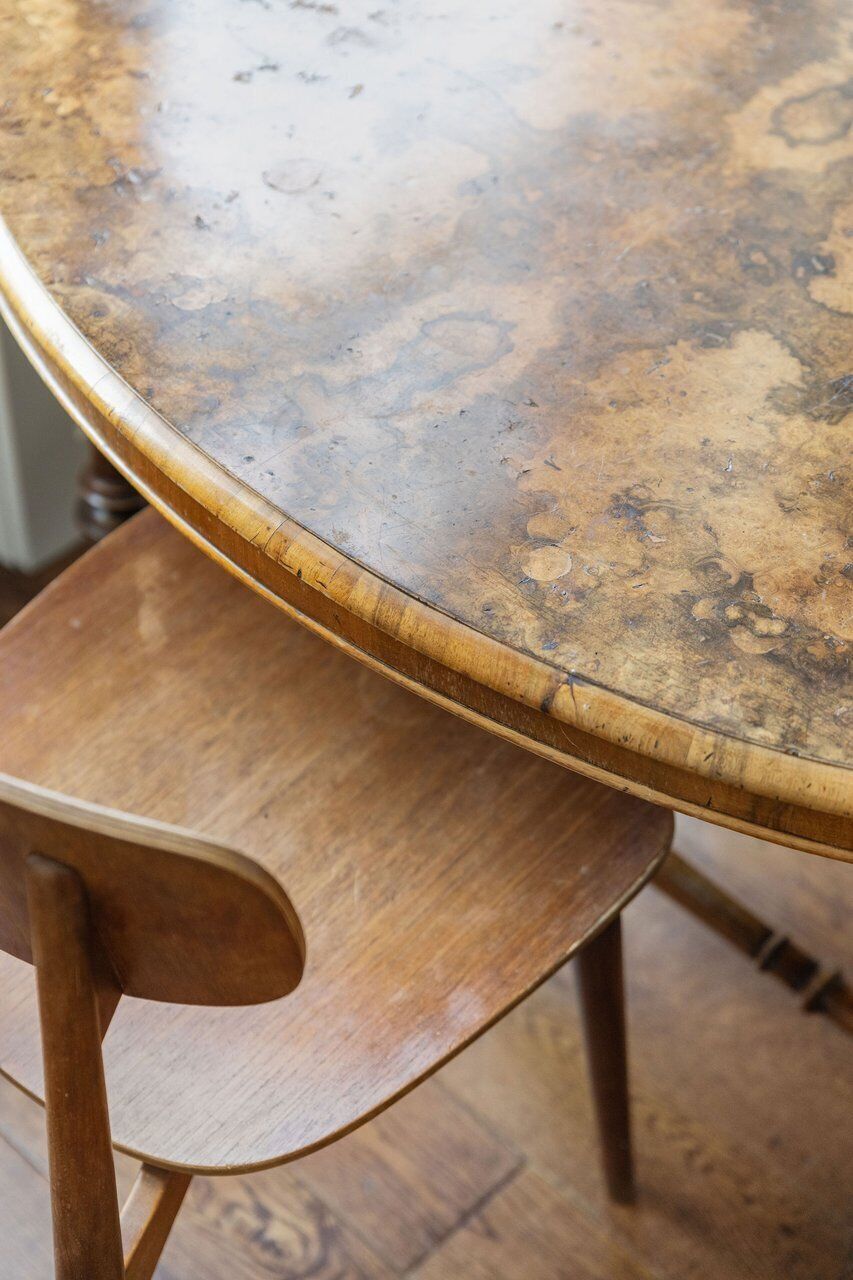 Una mesa redonda de madera con superficie desgastada, junto a una silla de madera.