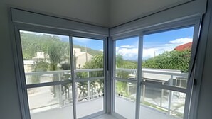 A room with large sliding glass doors leading to an outdoor balcony with a view of greenery and buildings. - Diamond Riviera - Casa Nova a 30m da Praia da Ferrugem (Garopaba)