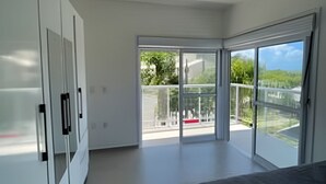 A modern bedroom with a large bed, a wardrobe, and a balcony with a view. - Diamond Riviera - Casa Nova a 30m da Praia da Ferrugem (Garopaba)