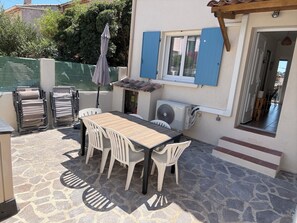 Eine Terrasse mit Tisch und Stühlen, einer Klimaanlage und einem überdachten Sitzbereich.