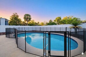 A swimming pool with a safety fence, surrounded by a white wall and trees. - Summer Escape .Heated Pool + Game Room & Sleeps 10 (Altamonte Springs)
