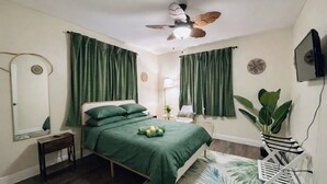 Une chambre à coucher avec un lit, un ventilateur de plafond, une télévision, une plante et un miroir.