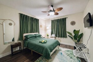 A bedroom with a bed, a ceiling fan, a TV, a plant, and a mirror. - Summer Escape .Heated Pool + Game Room & Sleeps 10 (Altamonte Springs)