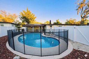 Ein runder Pool mit schwarzem Zaun, umgeben von einem weißen Zaun, und ein Haus im Hintergrund.