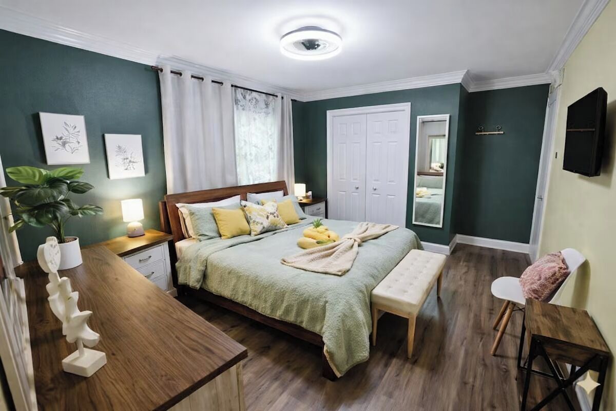 A bedroom with a bed, bedside tables, a bench, a mirror, and a wall-mounted TV.