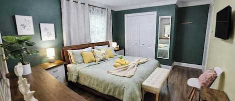 A bedroom with a bed, bedside tables, a bench, a mirror, and a wall-mounted TV.