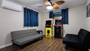 Une pièce avec un canapé gris, un canapé noir, un ventilateur de plafond et un distributeur automatique.