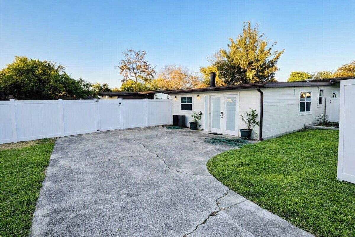 A residential property with a concrete driveway, a white fence, and a small lawn area.