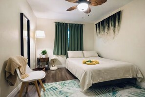 A bedroom with a bed, a chair, a desk, a lamp, and a ceiling fan.