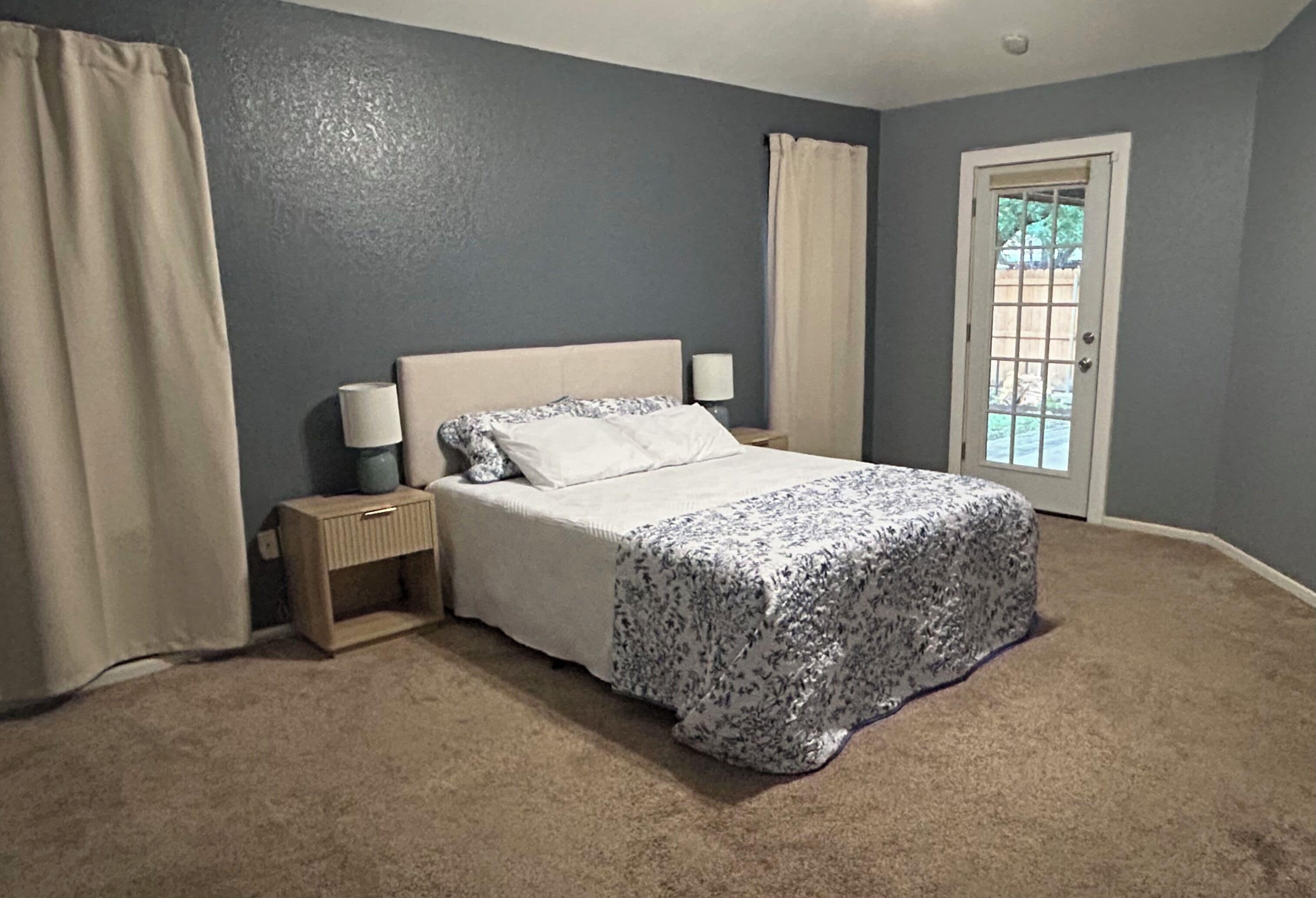 Un dormitorio con cama, mesita de noche y puerta a un balcón.