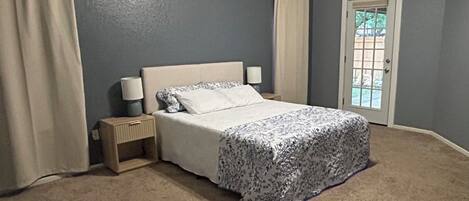 Un dormitorio con cama, mesita de noche y puerta a un balcón.