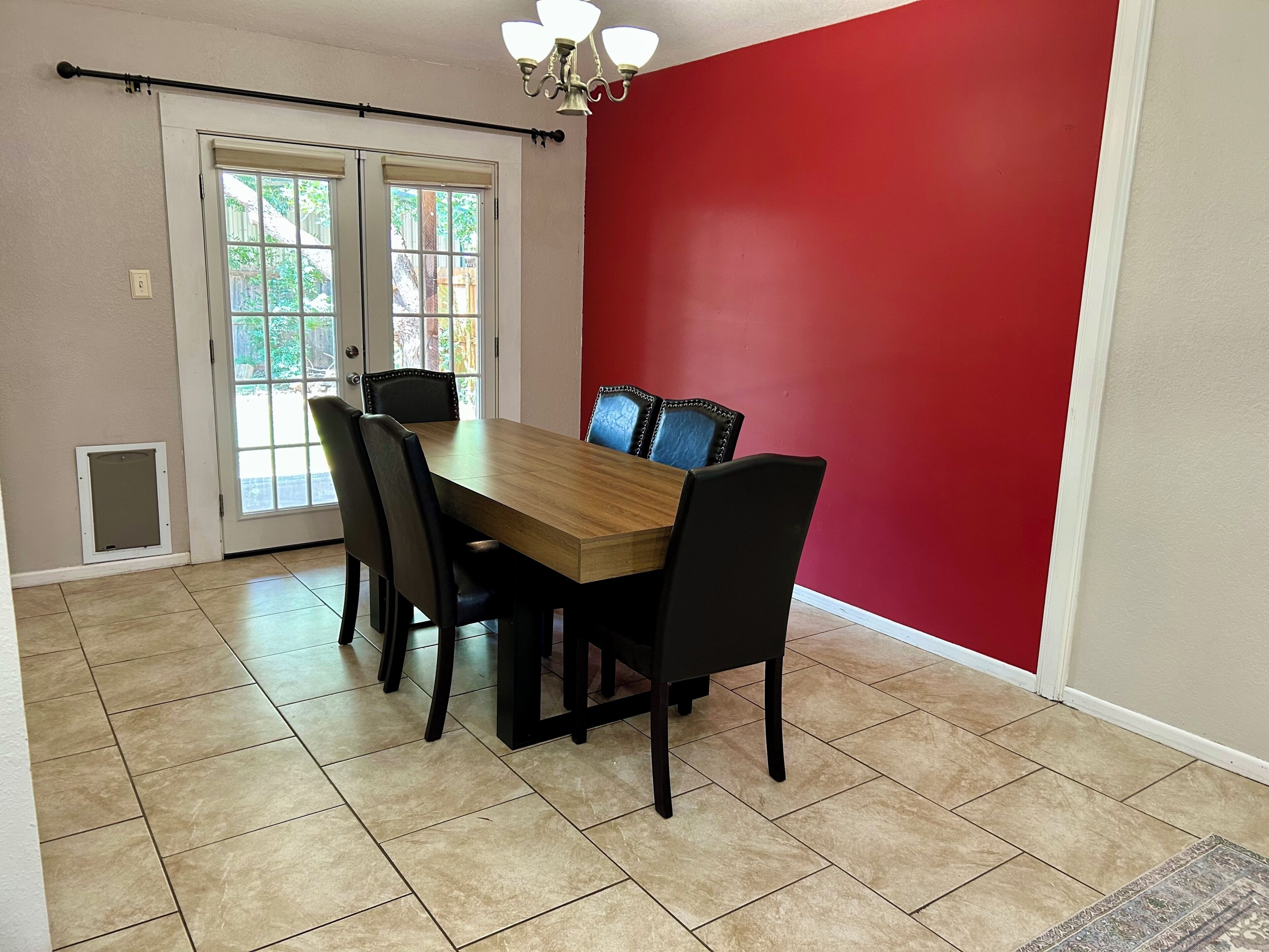 Un coin repas avec une table en bois et des chaises noires, un mur d’accent rouge et une porte-fenêtre coulissante donnant sur un jardin.