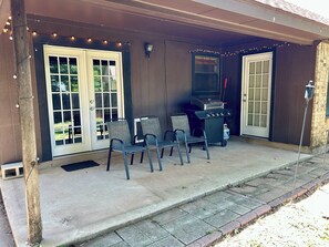 A covered patio with a grill, chairs, and string lights.