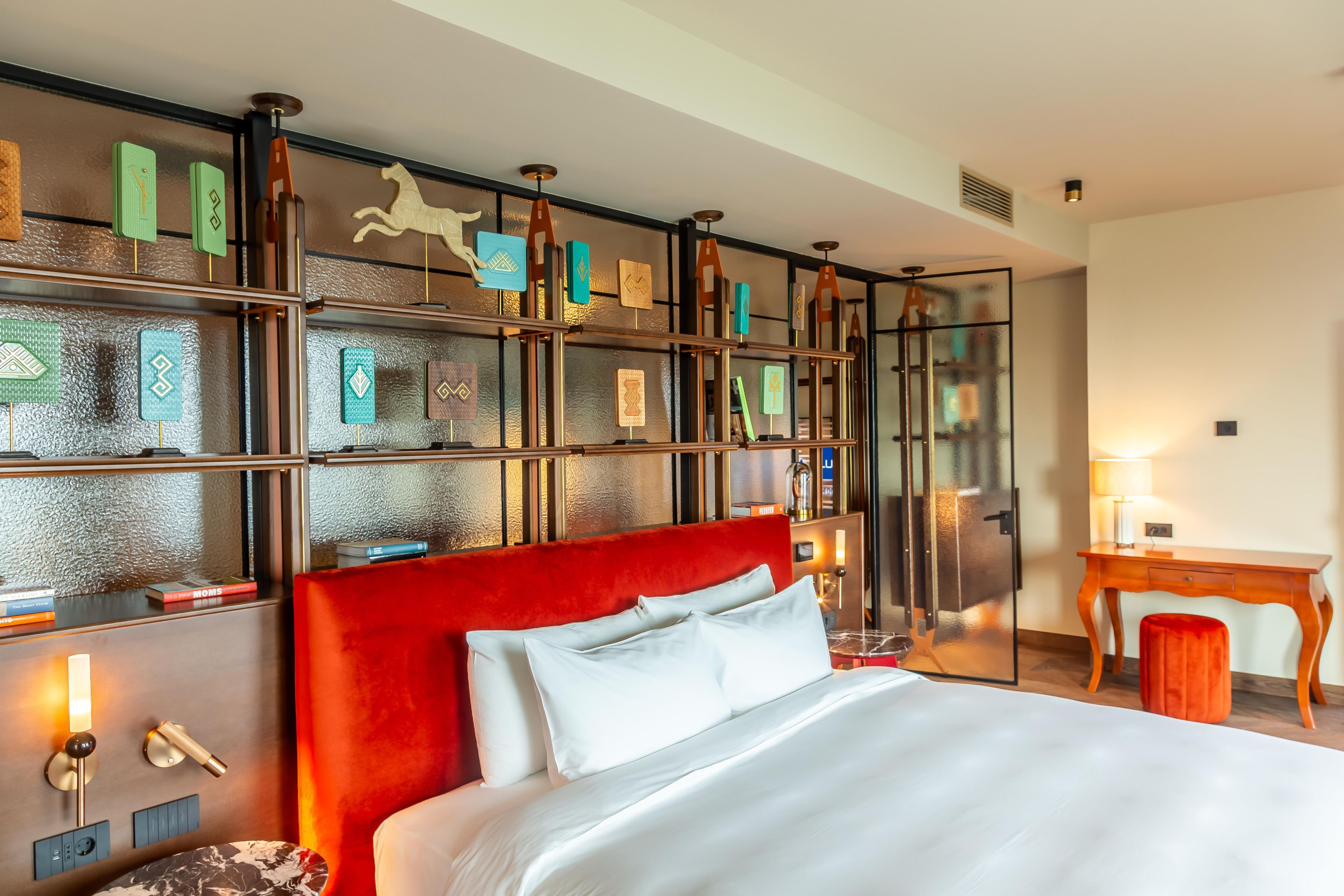 A hotel room with a large bed, a desk, and a bookshelf with decorative items.