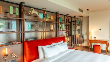 A hotel room with a large bed, a desk, and a bookshelf with decorative items.