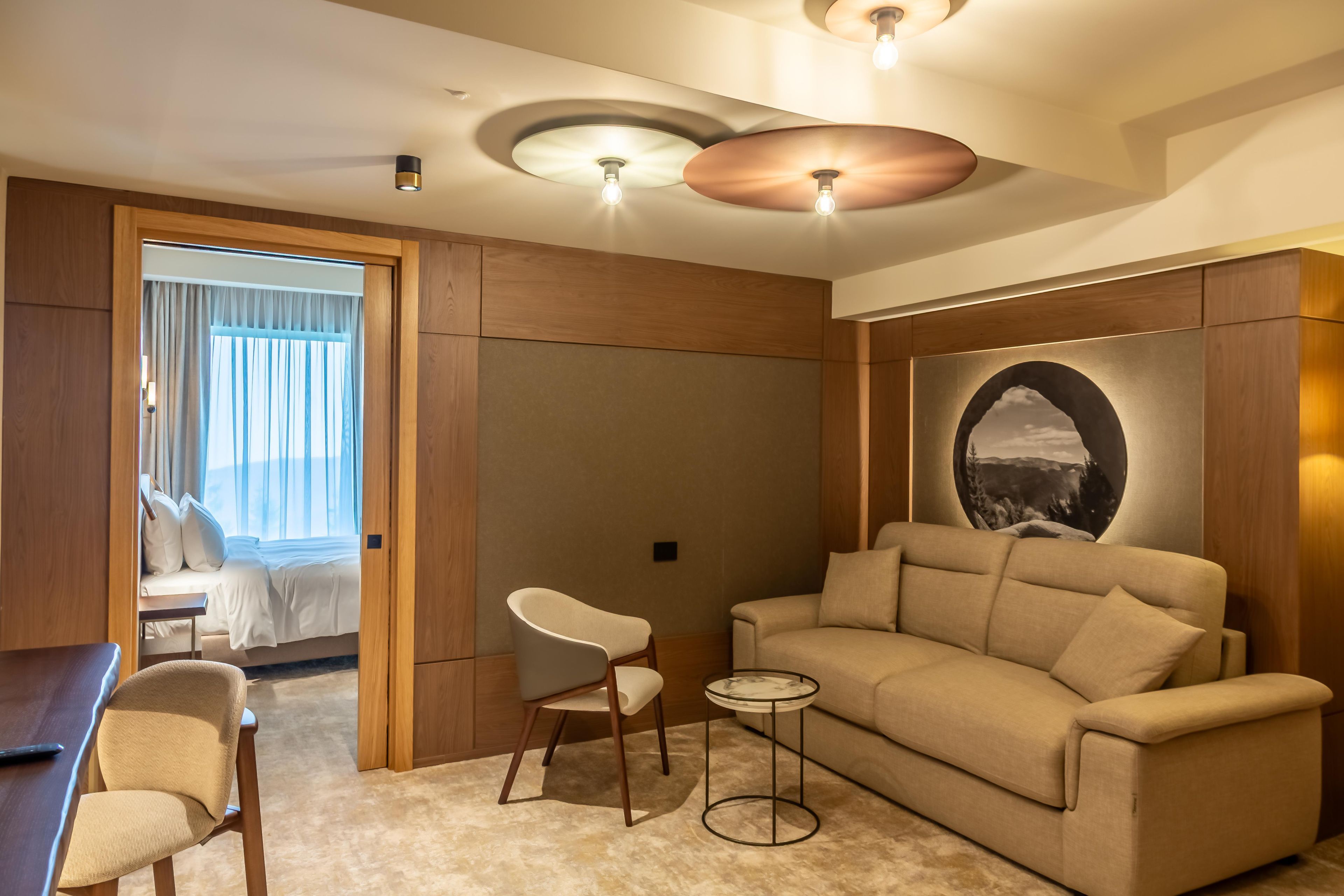 A modern hotel room with a sofa, a small side table, a chair, and a bed with curtains.