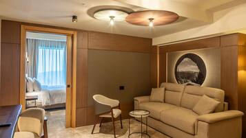 A modern hotel room with a sofa, a small side table, a chair, and a bed with curtains.