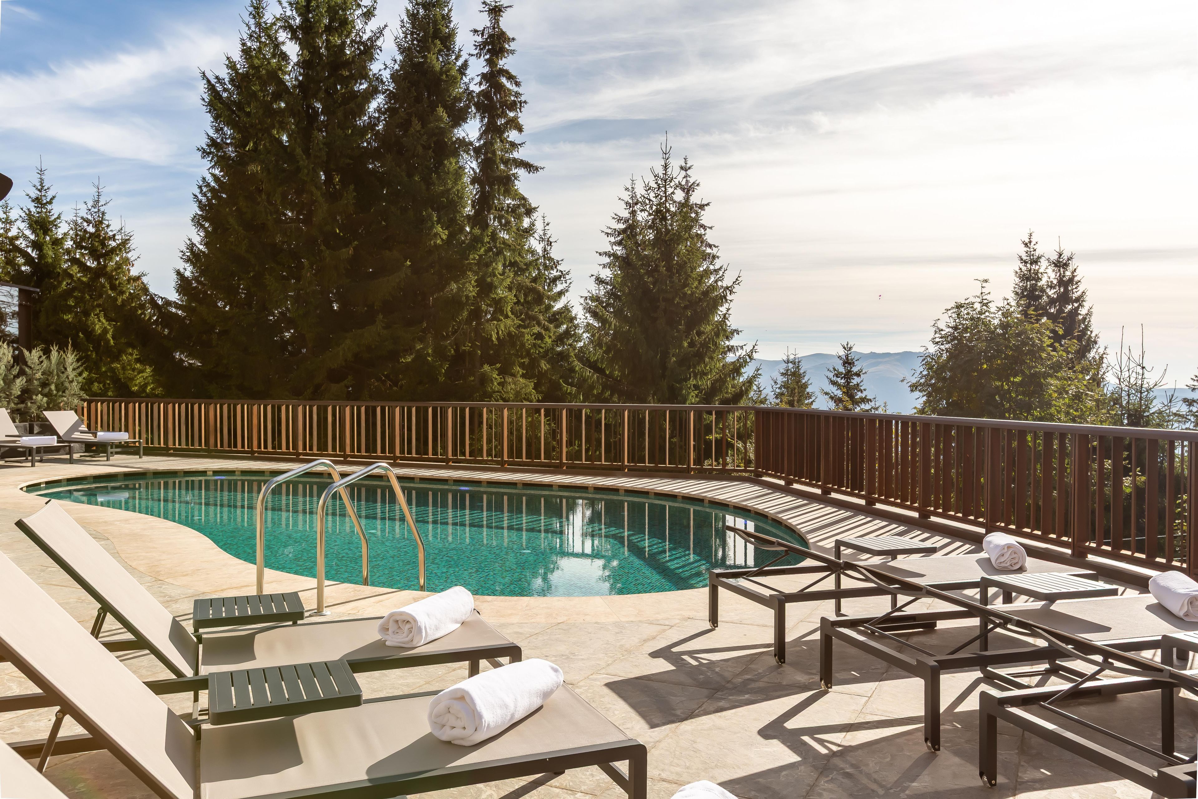 A poolside area with lounge chairs, a pool, and a wooden deck overlooking a mountainous landscape.