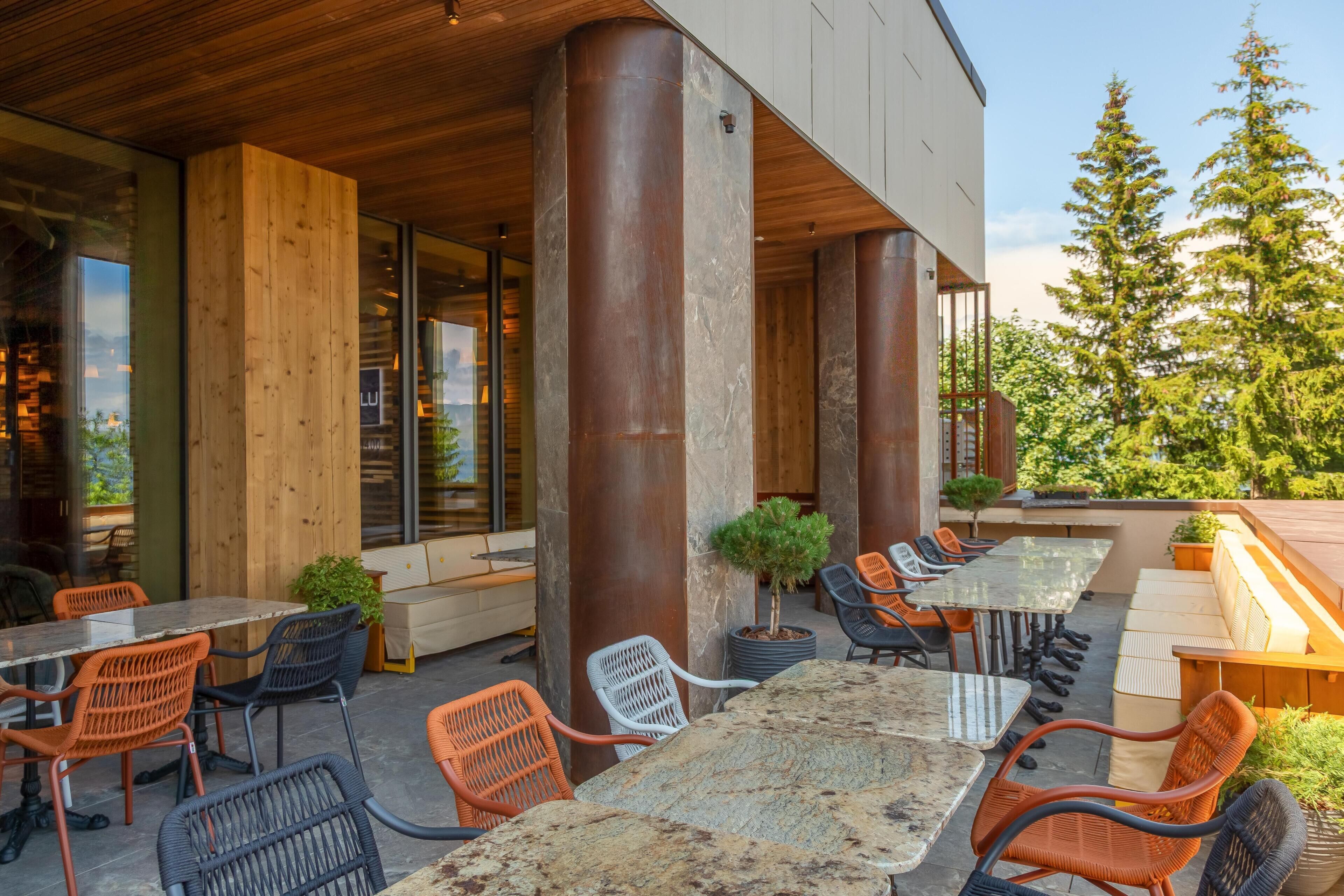 Un espace extérieur aménagé avec des tables et des chaises, de grandes colonnes et une vue sur les arbres.