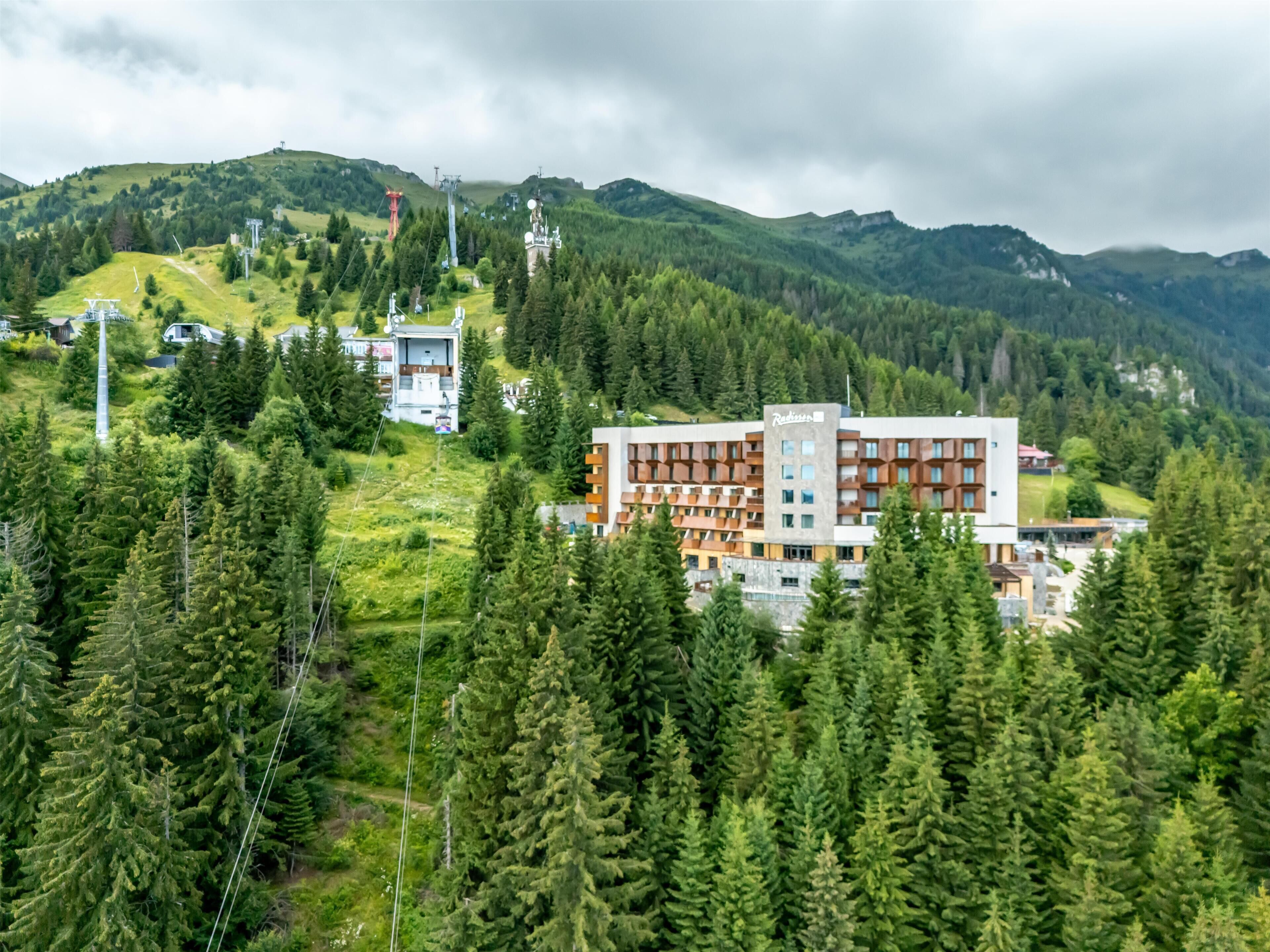 A hotel with a modern design, surrounded by dense forest and mountains.