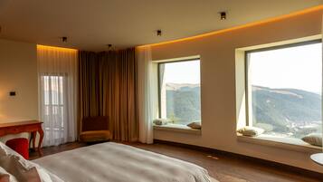 Habitación de hotel con una cama grande, un escritorio y una silla. Dos ventanas ofrecen vistas a la montaña.