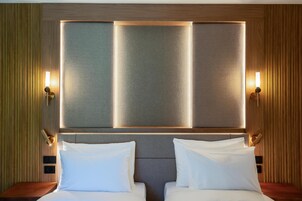Habitación de hotel con una cama grande, dos mesitas de noche y un aplique de pared.