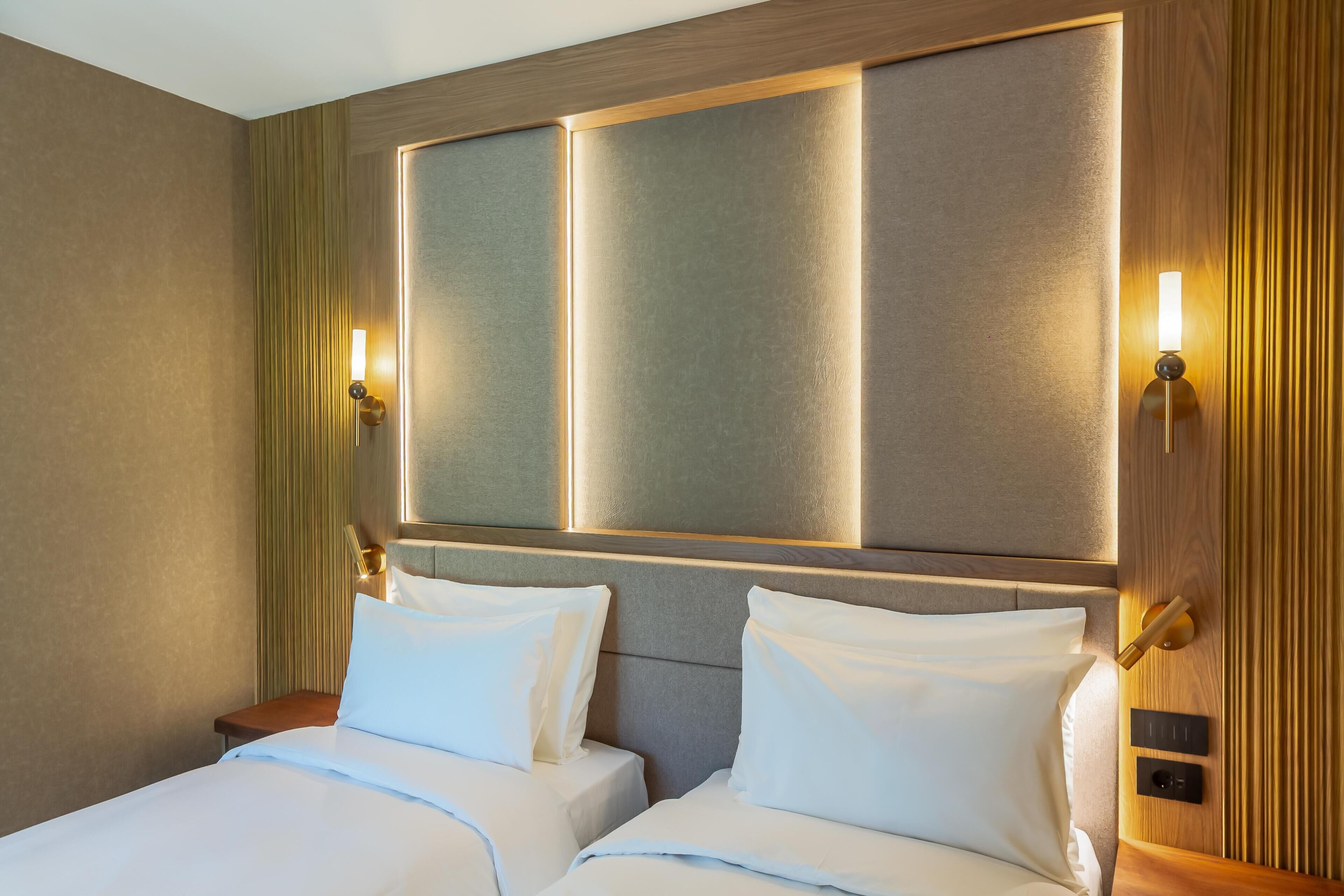A hotel room with a large bed, two bedside tables, and wall-mounted lamps.