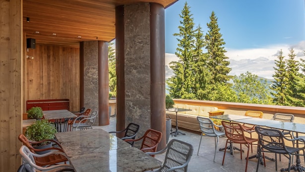 Un patio al aire libre con suelo de madera, pilares de piedra y diferentes opciones de mobiliario, incluyendo mesas y sillas.
