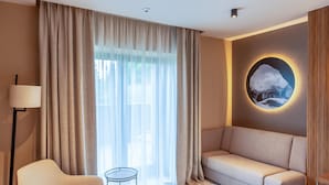 Una sala moderna con un sofá, una butaca, una mesita redonda y un ventanal con cortinas translúcidas.