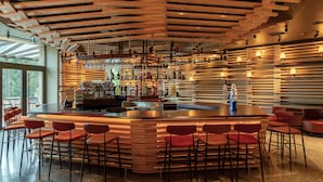 Un área de bar moderna con una isla central, taburetes y una variedad de botellas y vasos.