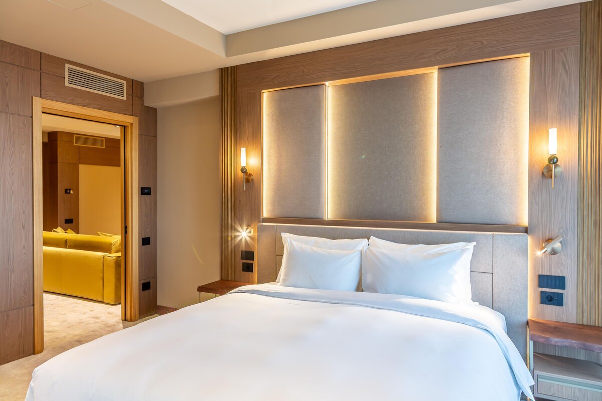 A hotel room with a large bed, a wooden headboard, and a nightstand with a lamp.