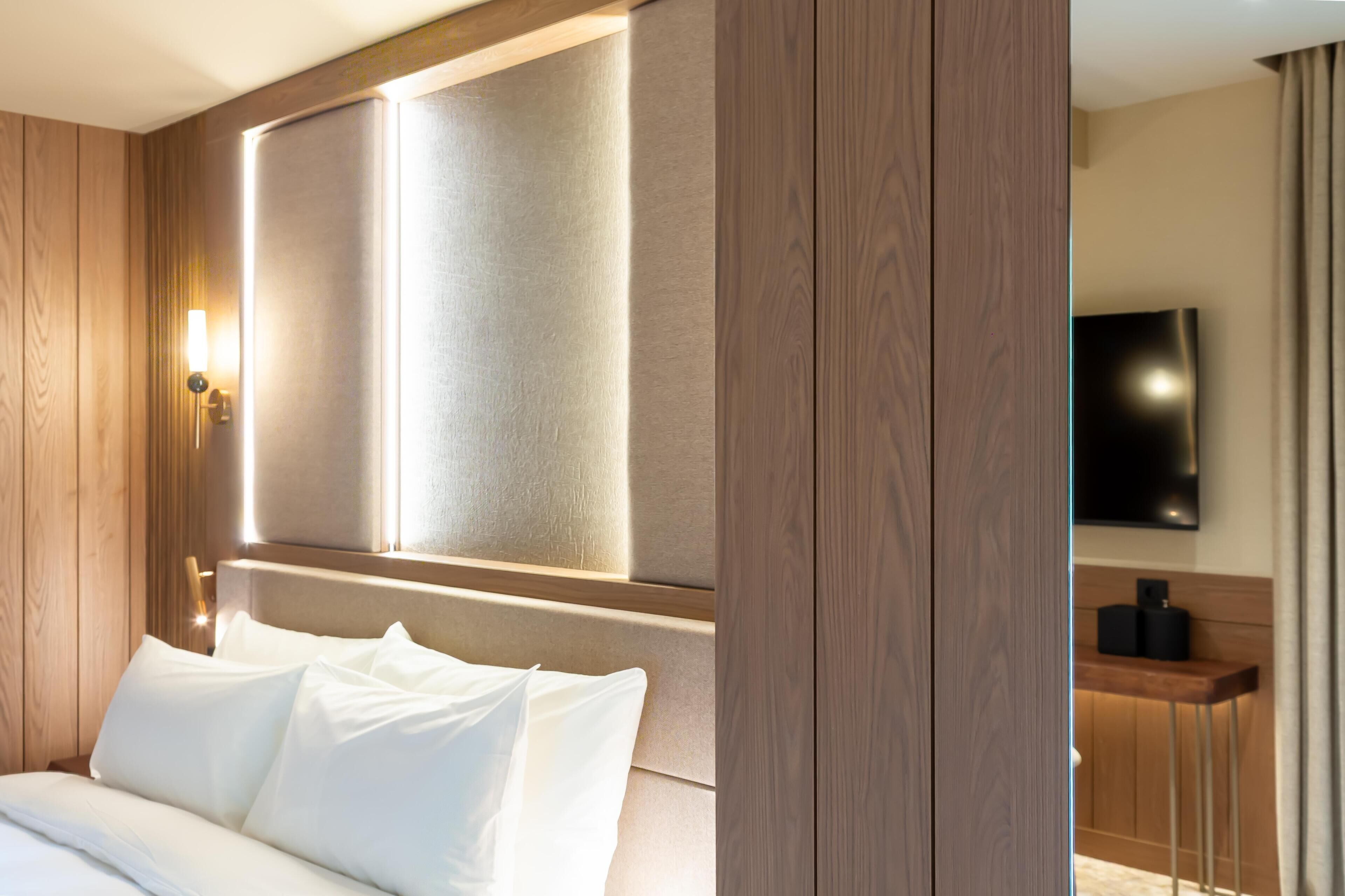 Habitación de hotel con cama, televisor de pantalla plana en la pared y cabecero de madera.