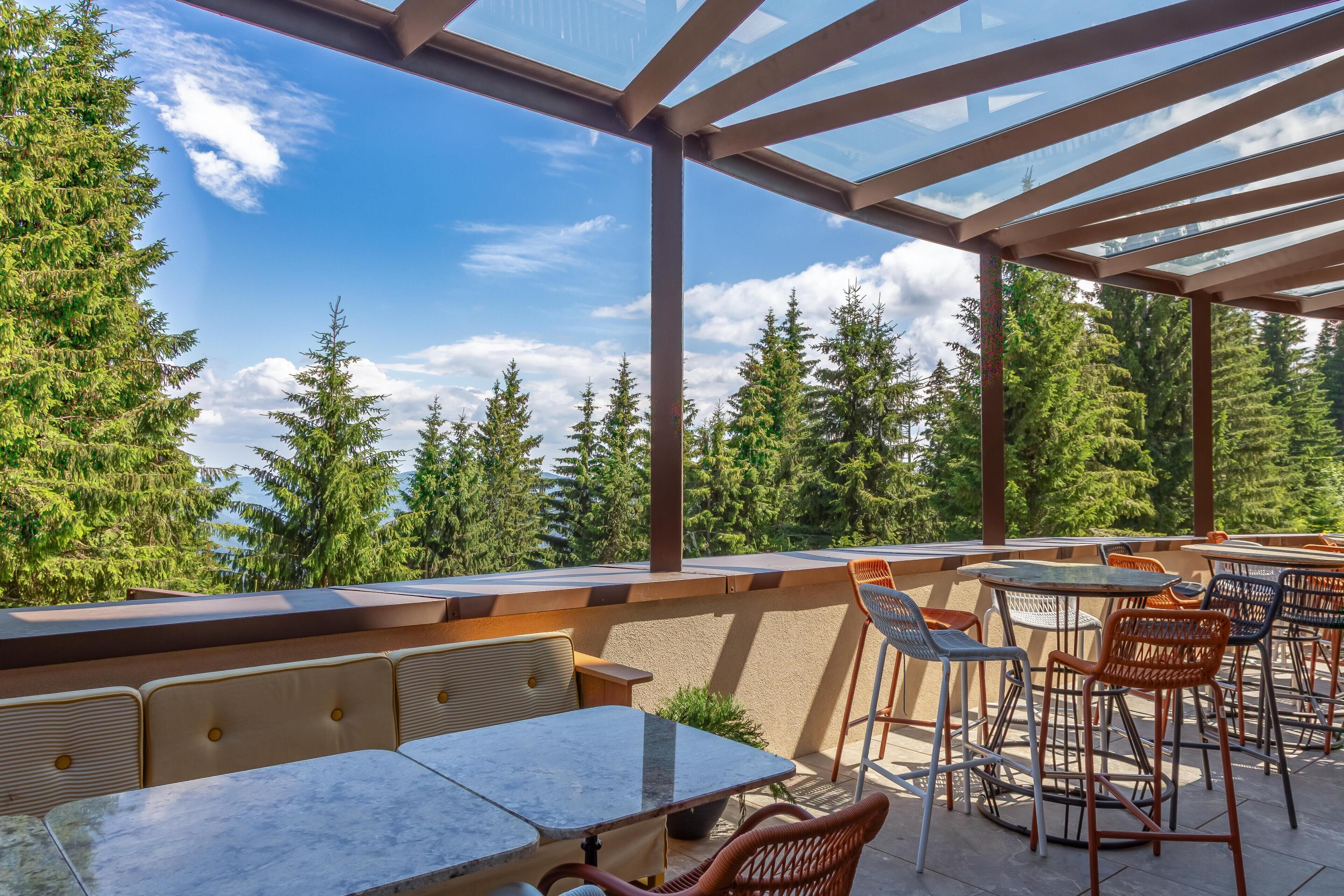 Un patio al aire libre con mesas y sillas, con vistas a un área boscosa.